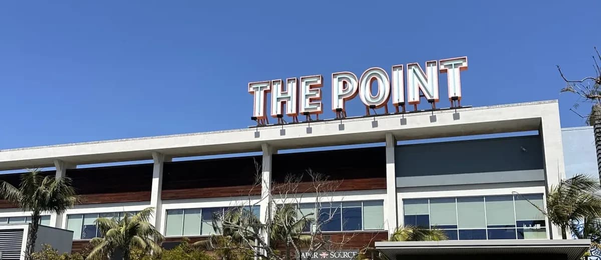 An outdoor lifestyle shopping center with storefronts, an open lawn, and palm trees